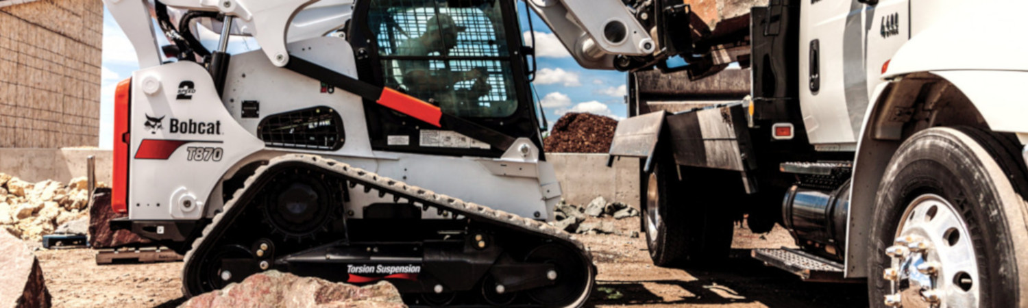 A black, orange, and white Bobcat® T870 skid steer loading rocks onto a truck.