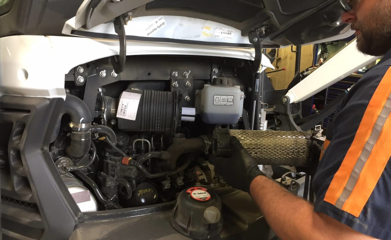 A man working on the engine of a piece of construction equipment.
